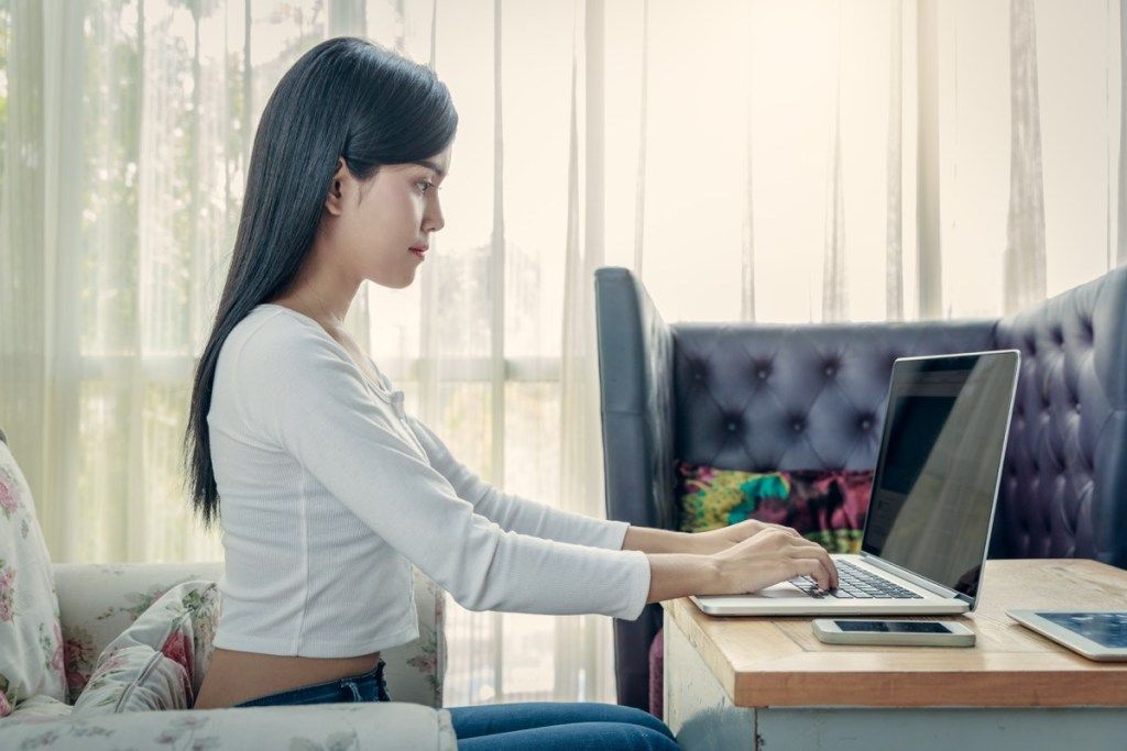 nainen istuu suoraan käytettäessä kannettavaa tietokonetta