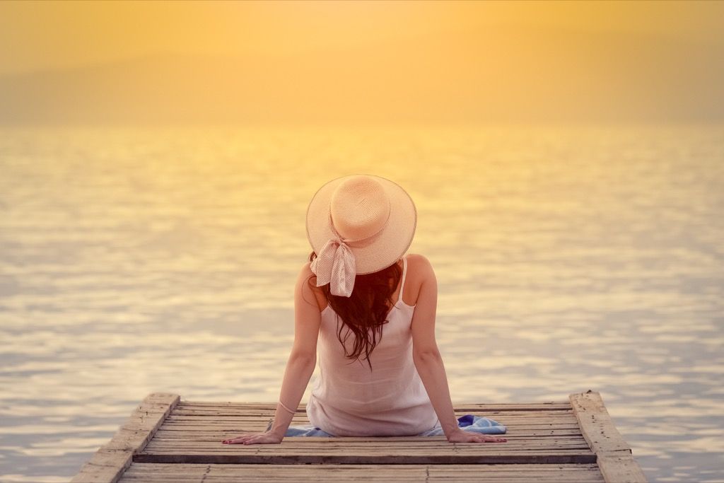nainen istuu telakalla auringonlaskun aikaan