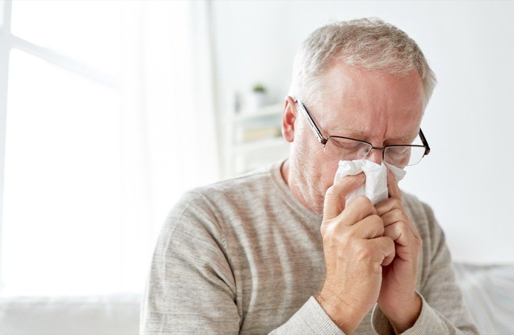 Hombre mayor con un resfriado sonándose la nariz con un pañuelo