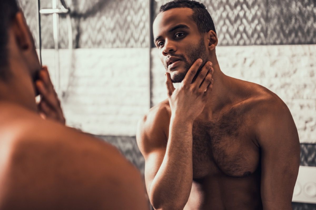 Jeune homme torse nu regardant dans le miroir, hydratant qui aide à repousser le vieillissement