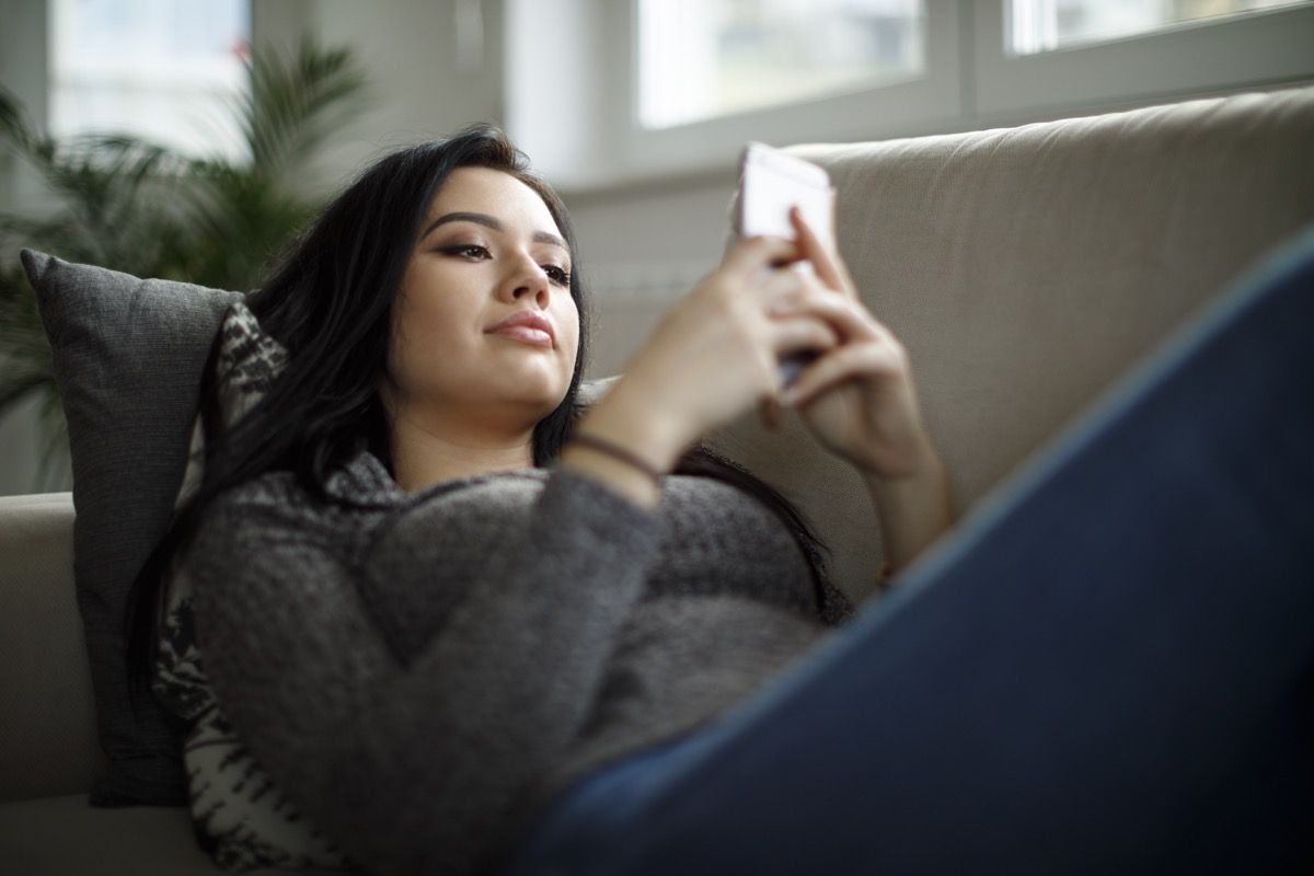 امرأة آسيوية شابة texting على الأريكة