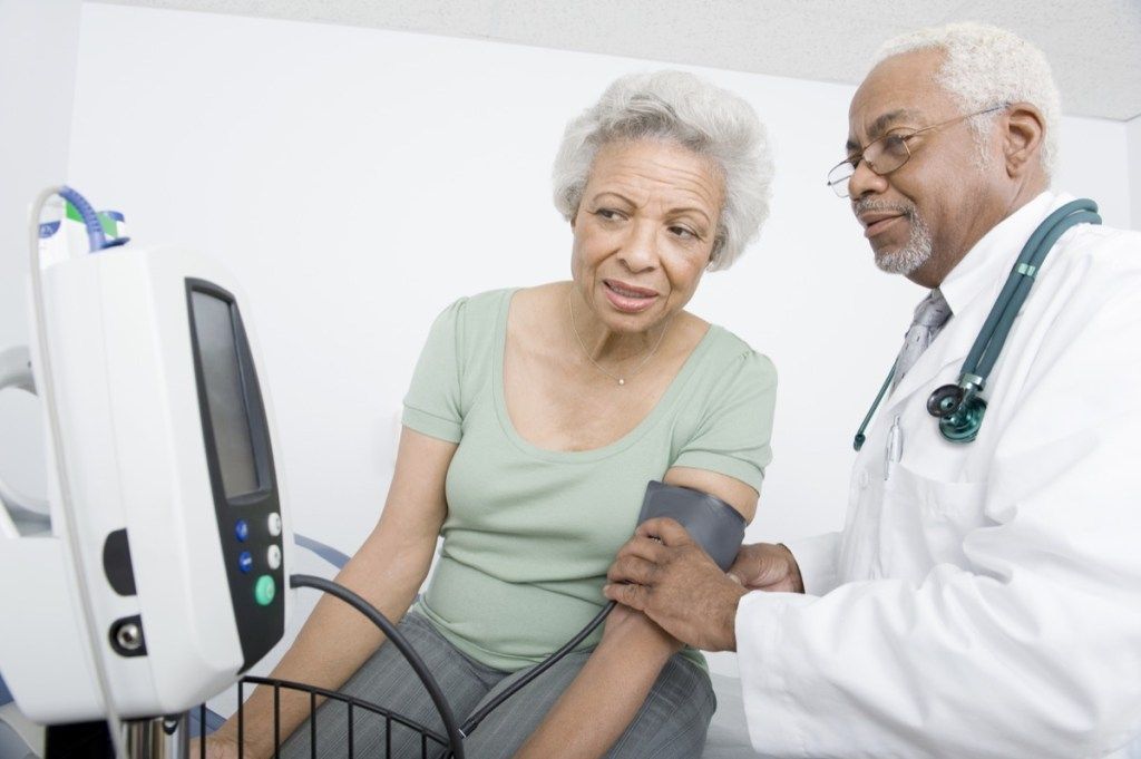 画面を見ながら血圧を測定している女性と医師、50歳以降の健康に関する質問