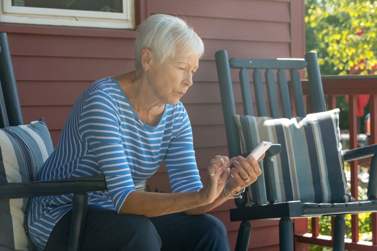 ältere weiße Frau, die draußen eine SMS schreibt, während sie besorgt aussieht