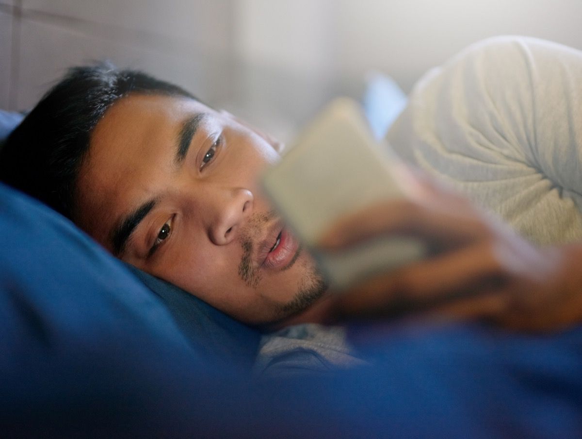 ベッドに横たわっているときに彼の携帯電話を見ている若い男のショット