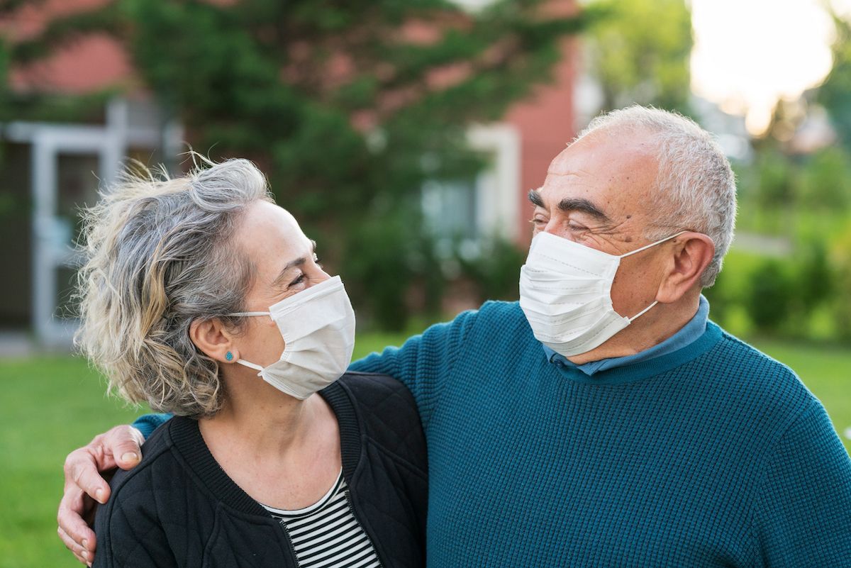 stariji par Par nosi kirurške maske i smiješi se jedni drugima