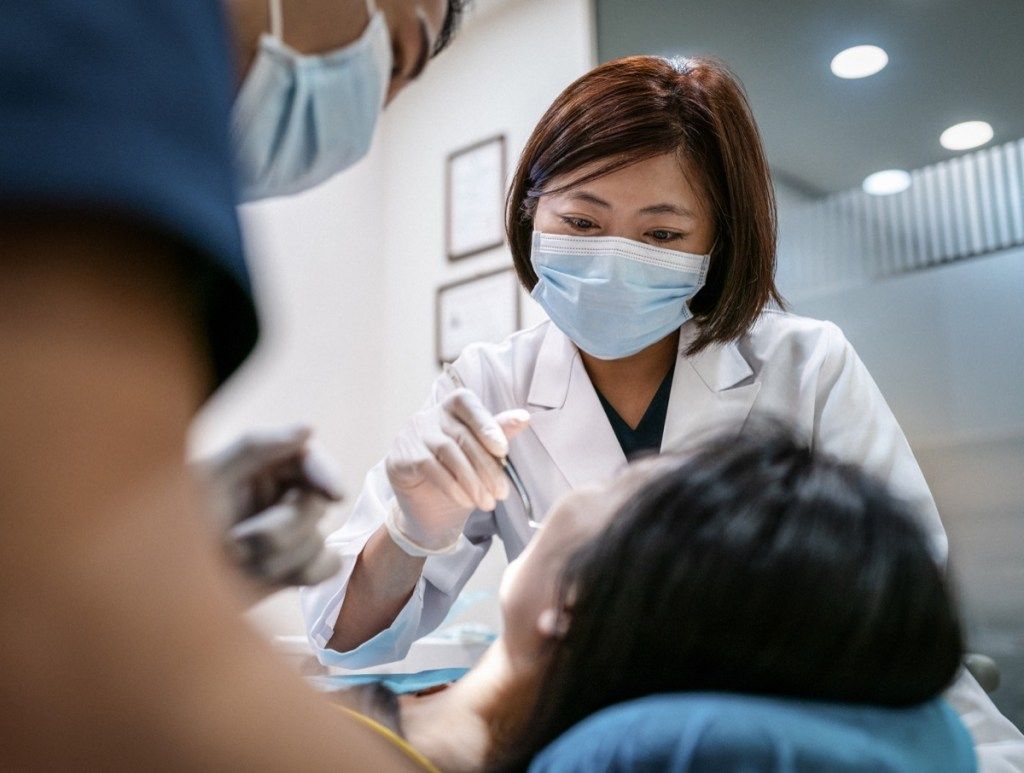 Tandläkare med manlig assistent som behandlar kvinnlig patient