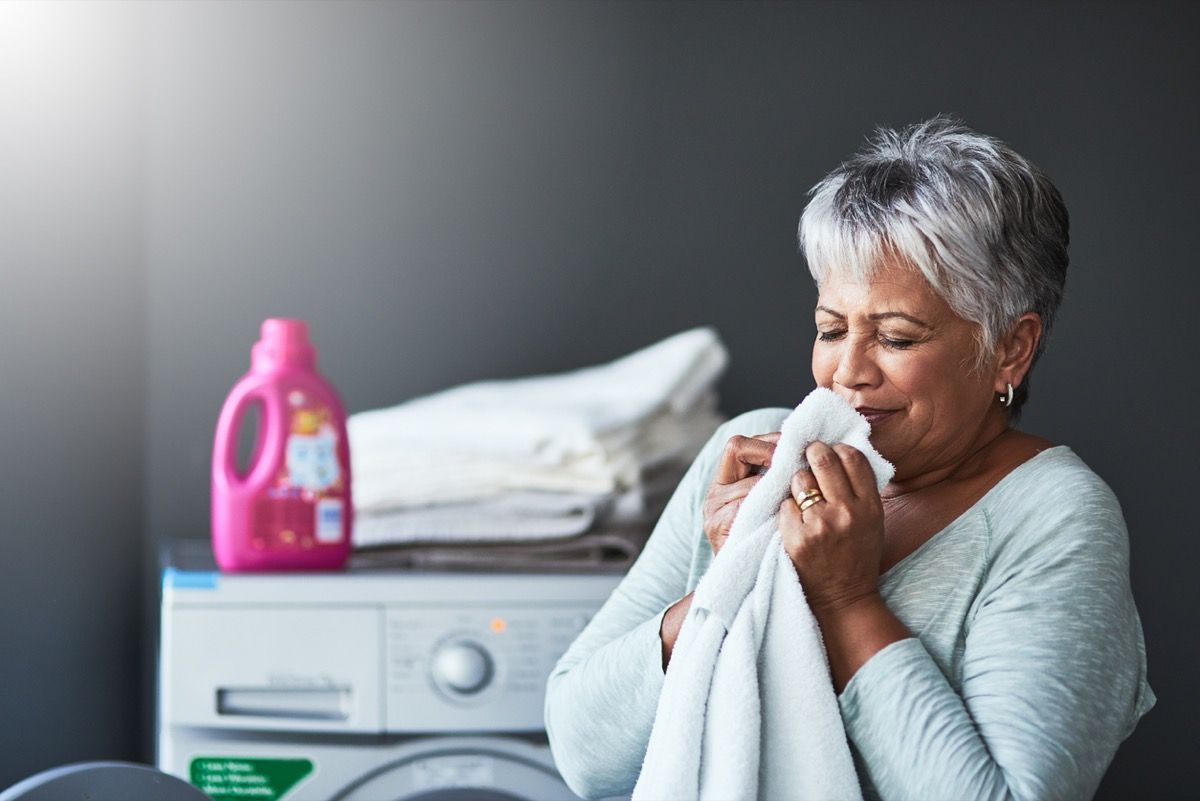 äldre latina kvinna som luktar en ny handduk nära tvättmaskinen