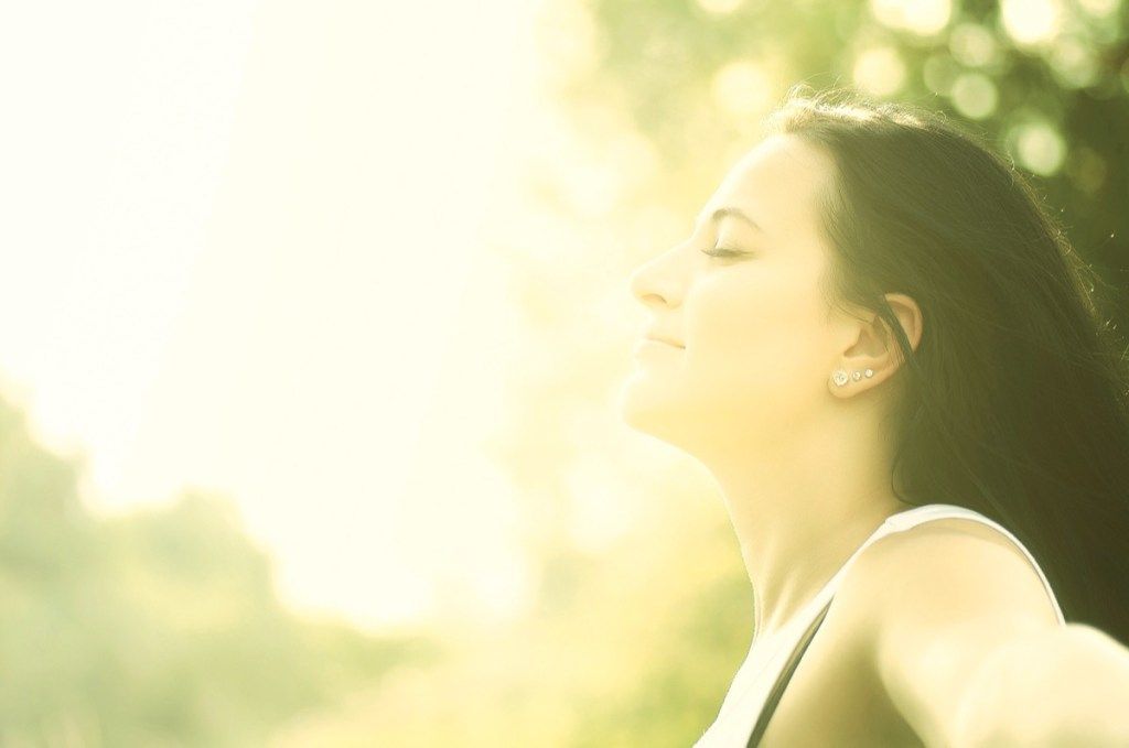 млада жена се радва на слънчеви лъчи в летния парк.