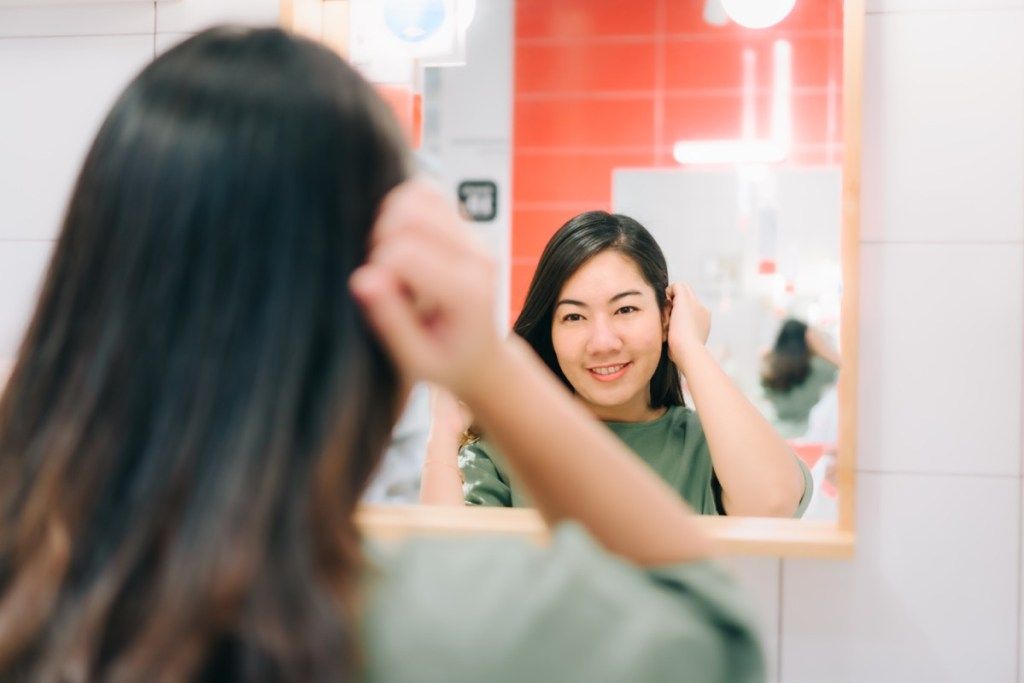 Phụ nữ châu Á đang nhìn mình phản chiếu trong gương
