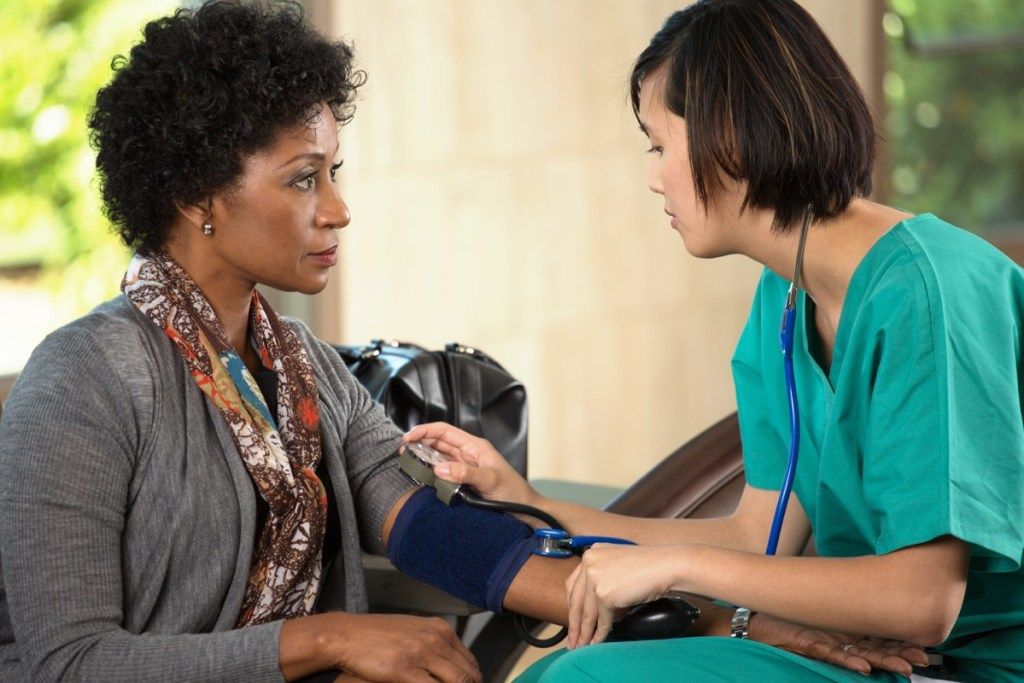 Жена при доктора, получаваща кръвно налягане Провери факти за рак на кожата