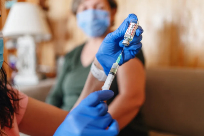   Allmennlege vaksinerer gammel pasient hjemme med kopiplass. Lege som gir injeksjon til eldre kvinne hjemme. Sykepleier holder sprøyten og bruker bomull før de lager Covid-19 eller koronavirusvaksine.