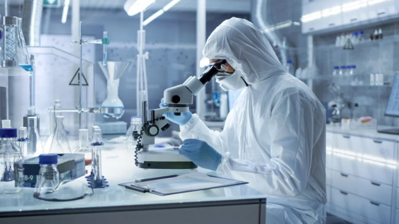   Znanstvenik koji završava studiju u laboratoriju gledajući u mikroskop noseći punu zaštitnu opremu
