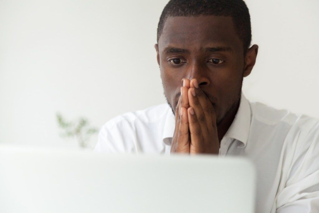 Чернокожият човек, седнал до компютъра си, чувства се стресиран и притеснен