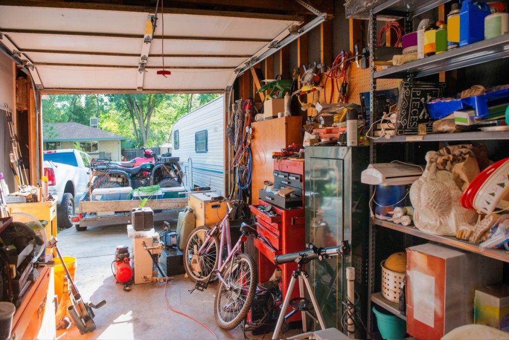 Ova je fotografija garaže obložene policama punim stvari koje se čuvaju kod kuće, uključujući alate, pribor za čišćenje, ukrase za odmor i sportsku opremu. Garažna vrata su otvorena.
