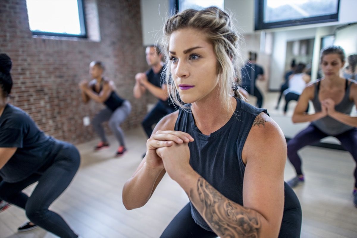 Forskellig gruppe unge voksne, der laver squats i fællesskab under en fitnessklasse