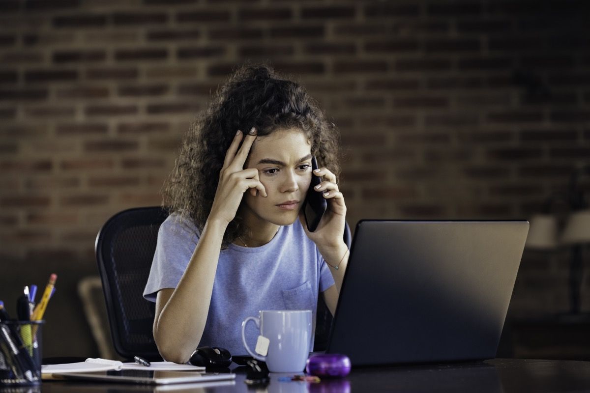 Arbetshem: orolig ung kvinna som använder bärbara datorn och arbetar hemma kontor. Låg nyckelplats fångad i ett lantligt kök.