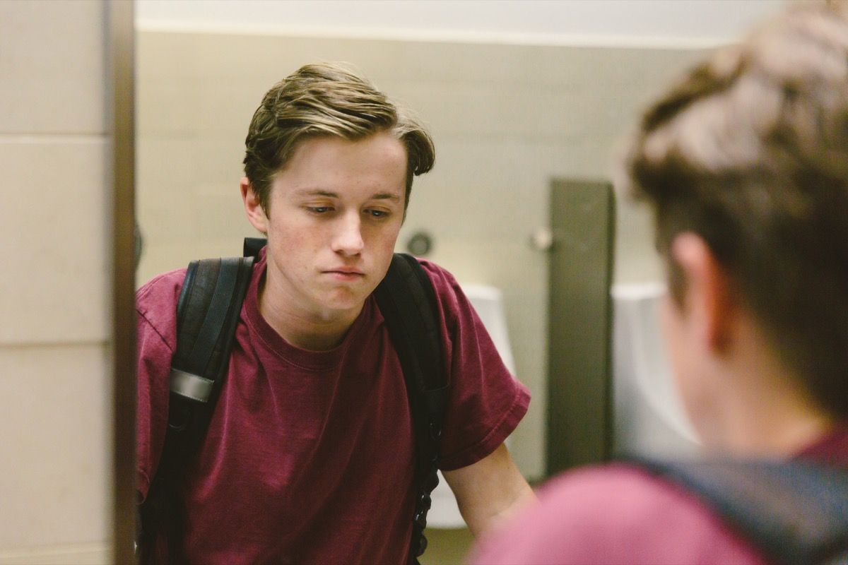 Sinh viên tuổi teen chán nản nhìn chằm chằm vào hình ảnh phản chiếu của mình trong gương trong phòng tắm một cách bất lực.