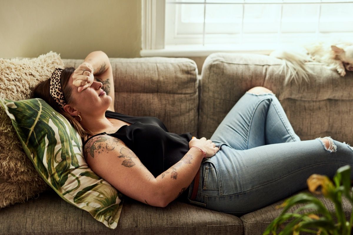 Кадър на млада жена, страдаща от стомашни спазми на дивана у дома