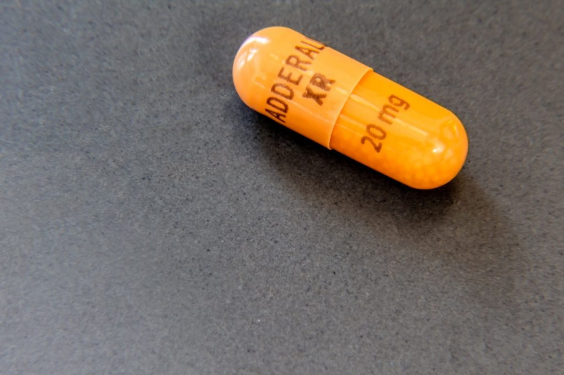   Enkel 20 mg kapsel av Adderall XR, et blandet amfetaminsalterstimulerende middel som brukes i psykiatrisk medisin for å behandle ADD, ADHD og narkolepsi, på en grå overflate.
