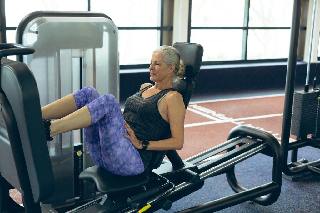Vyresnio amžiaus moteris sporto salėje naudoja kojų presavimo mašiną
