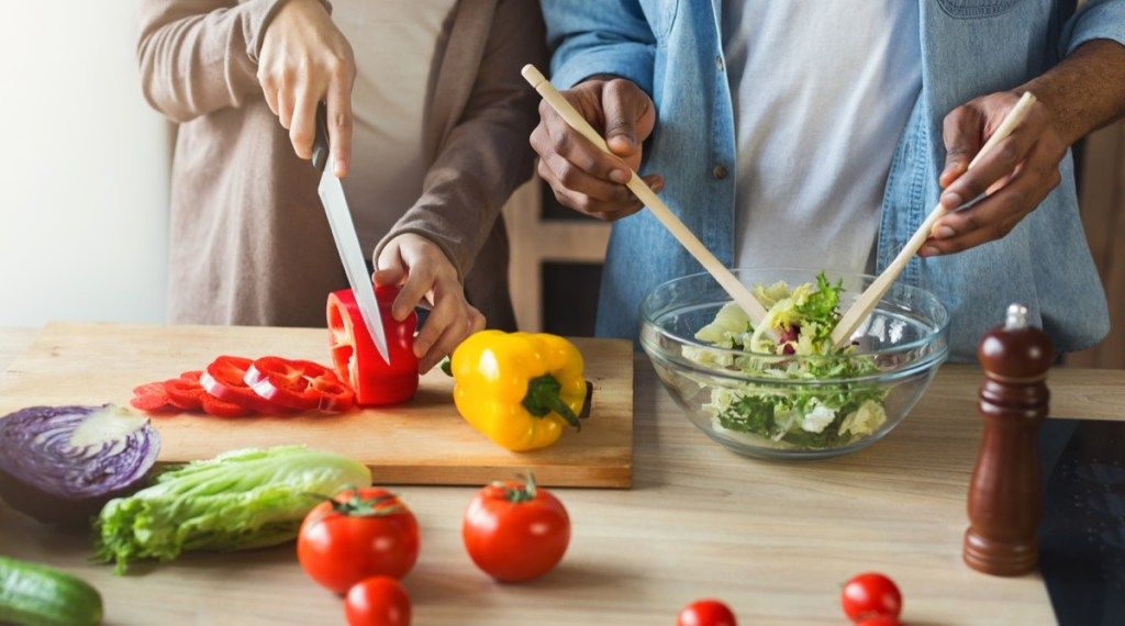 Un couple marié hache des légumes et prépare une salade dans une cuisine bien éclairée