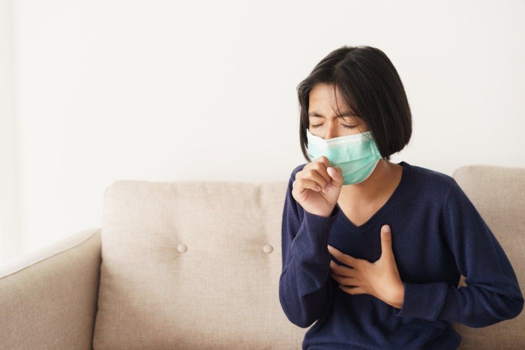 meitenes simptoms klepus un ir aizsargājošs ar medicīnisko masku, sēžot uz dīvāna, Āzijas bērns valkā aizsardzības maskas gripas vai covid-19 epidēmiju viesistabā mājās. Veselības un slimības koncepcija