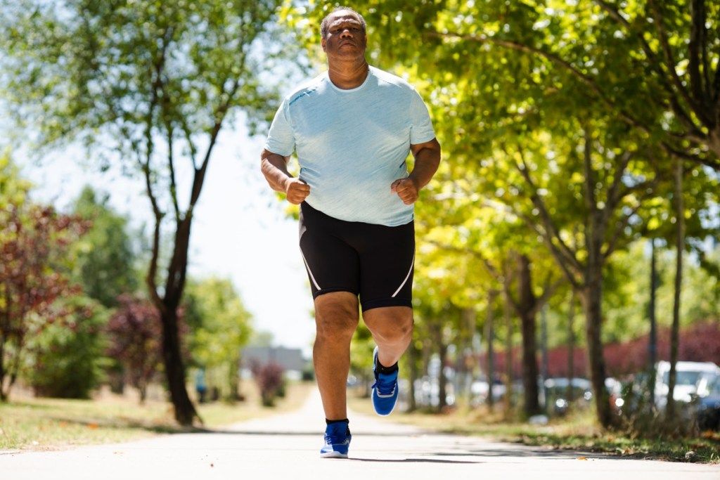Hombre negro con sobrepeso corriendo afuera haciendo algo de ejercicio en