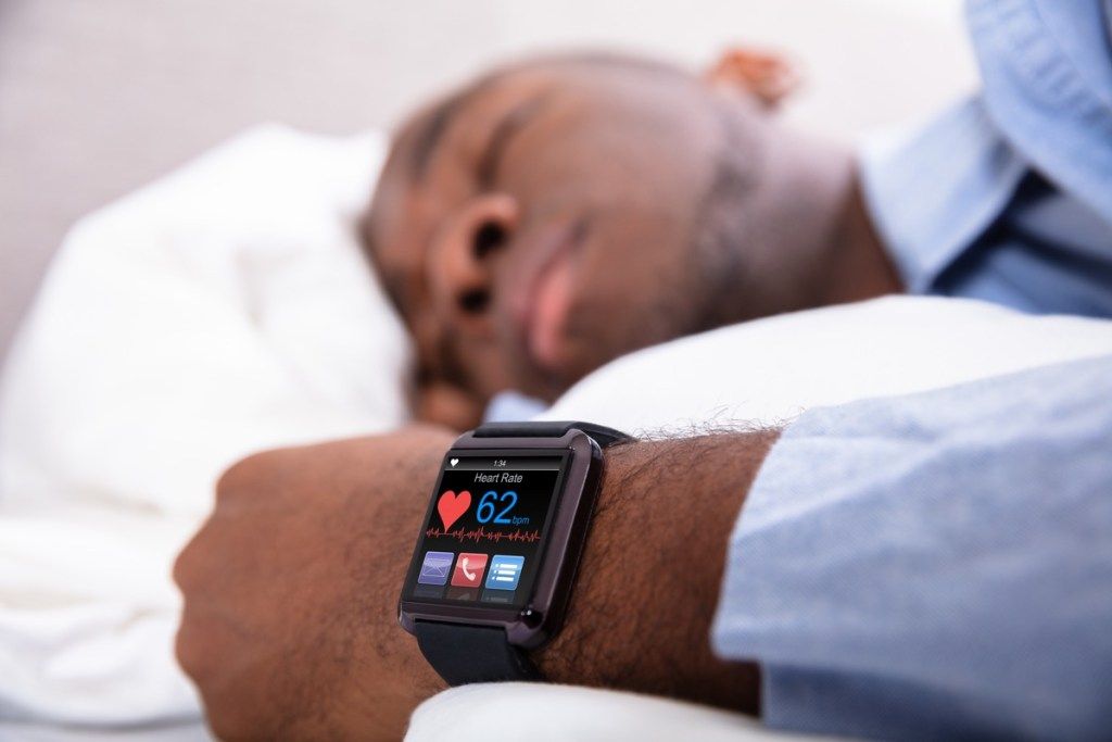 Едър план на мъж, който спи с интелигентен часовник в ръка, показващ пулса