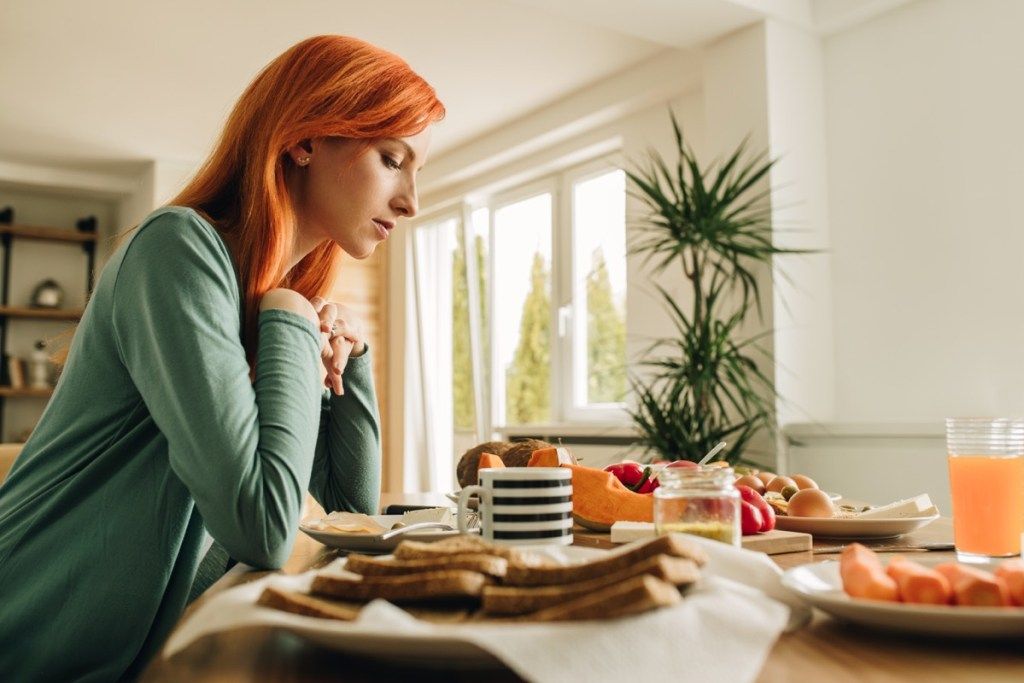 Yksinäinen punapää nainen istuu ruokapöydässä ja ajattelee jotain.