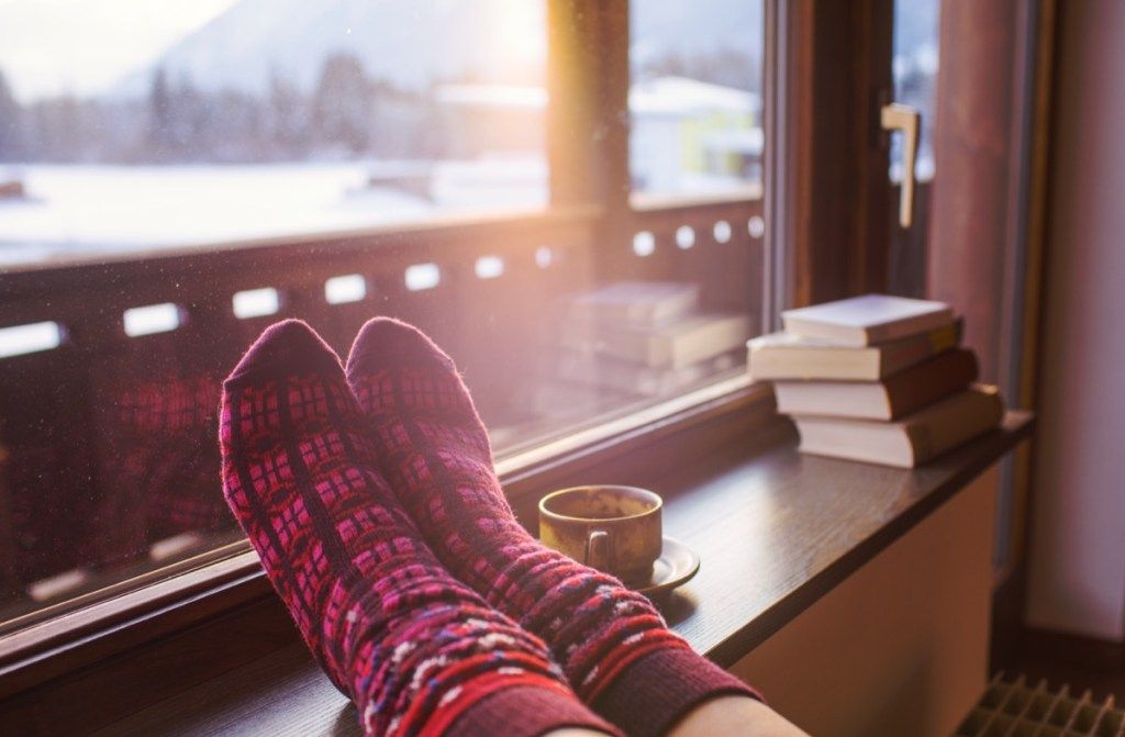 Des chaussettes sur un radiateur à côté de livres et une tasse de thé dans une maison en hiver