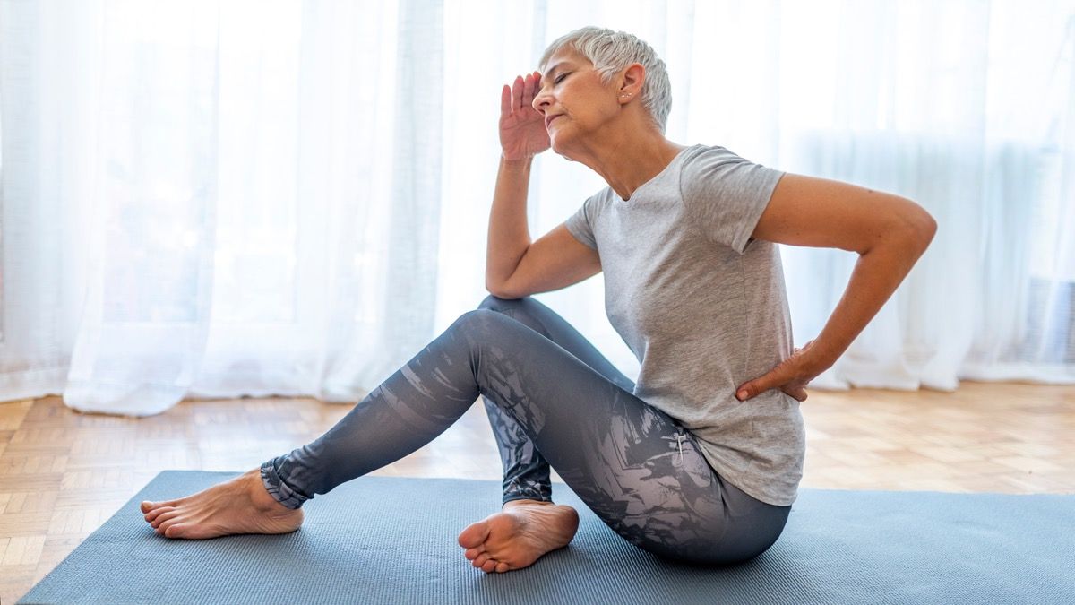 Sieviete ar muguras lejasdaļas sāpēm uz jogas paklāja