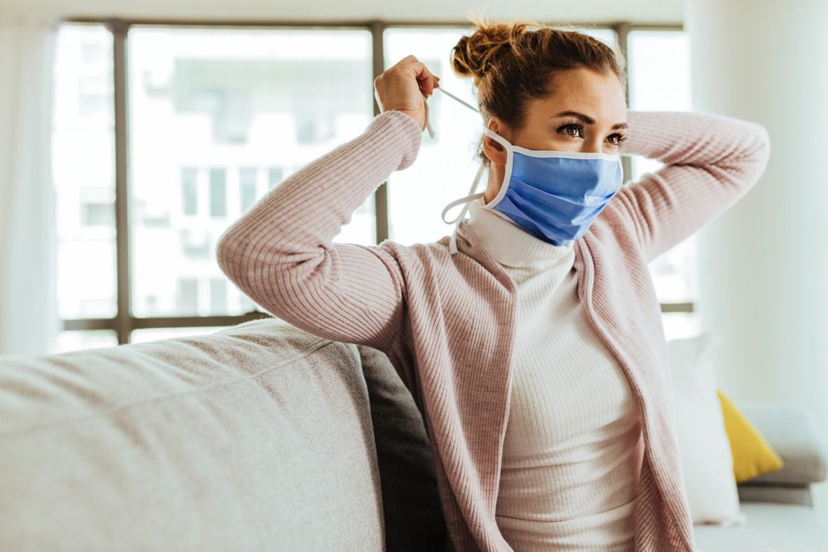 Млада жена која користи заштитну маску за лице код куће током пандемије коронавируса.