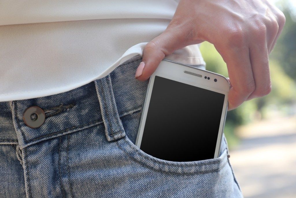 Pessoa colocando o telefone no bolso da calça jeans