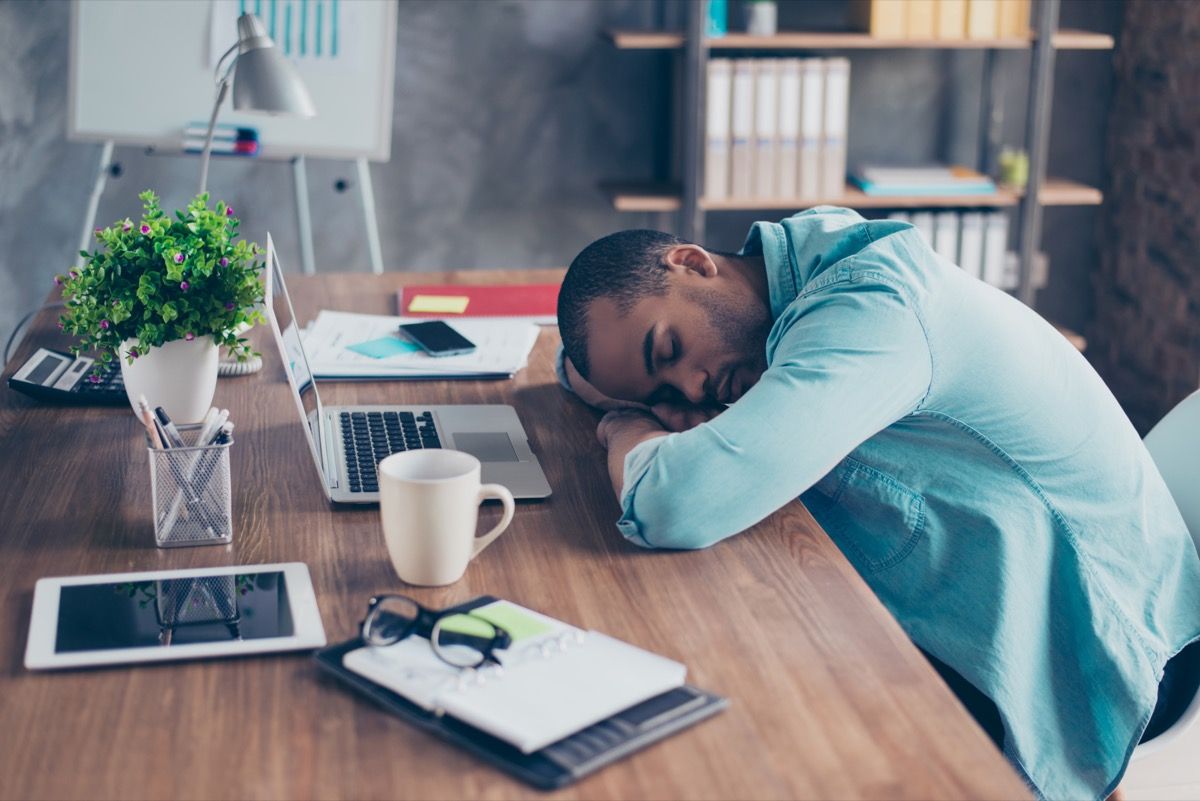 ένας άντρας που κοιμάται σε ένα γραφείο με φορητό υπολογιστή και ένα tablet μπροστά του