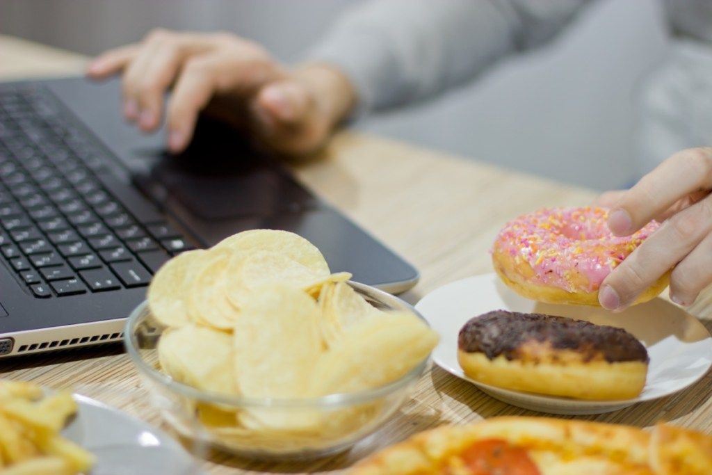 Frau, die Donuts und Chips während der Arbeit von zu Hause isst
