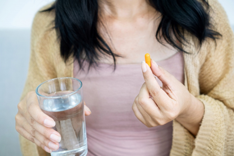   Frauenhand, die Kurkuma-Pille einnimmt, Mädchenhand, die Kurkuma-Pulver in Kapseln oder Curcumin-Kräutermedizin mit einem Glas Wasser hält, Behandlung von saurem Reflux-Problem