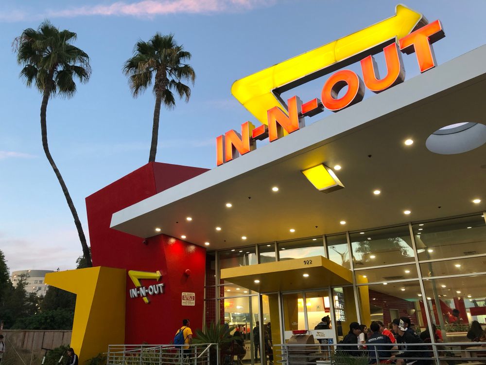 En In-N-Out Burger-beliggenhet ved solnedgang med palmer foran.