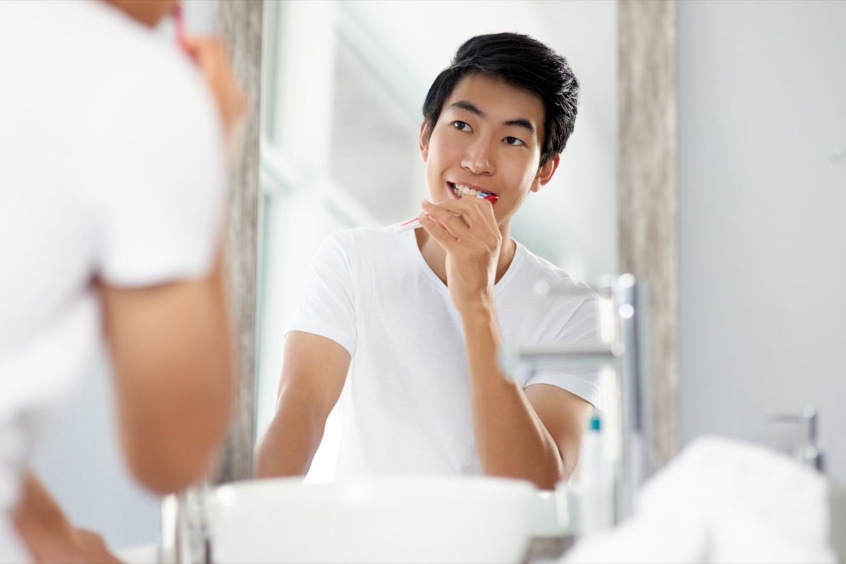 Кадър на красив млад мъж, който си мие зъбите в банята у дома