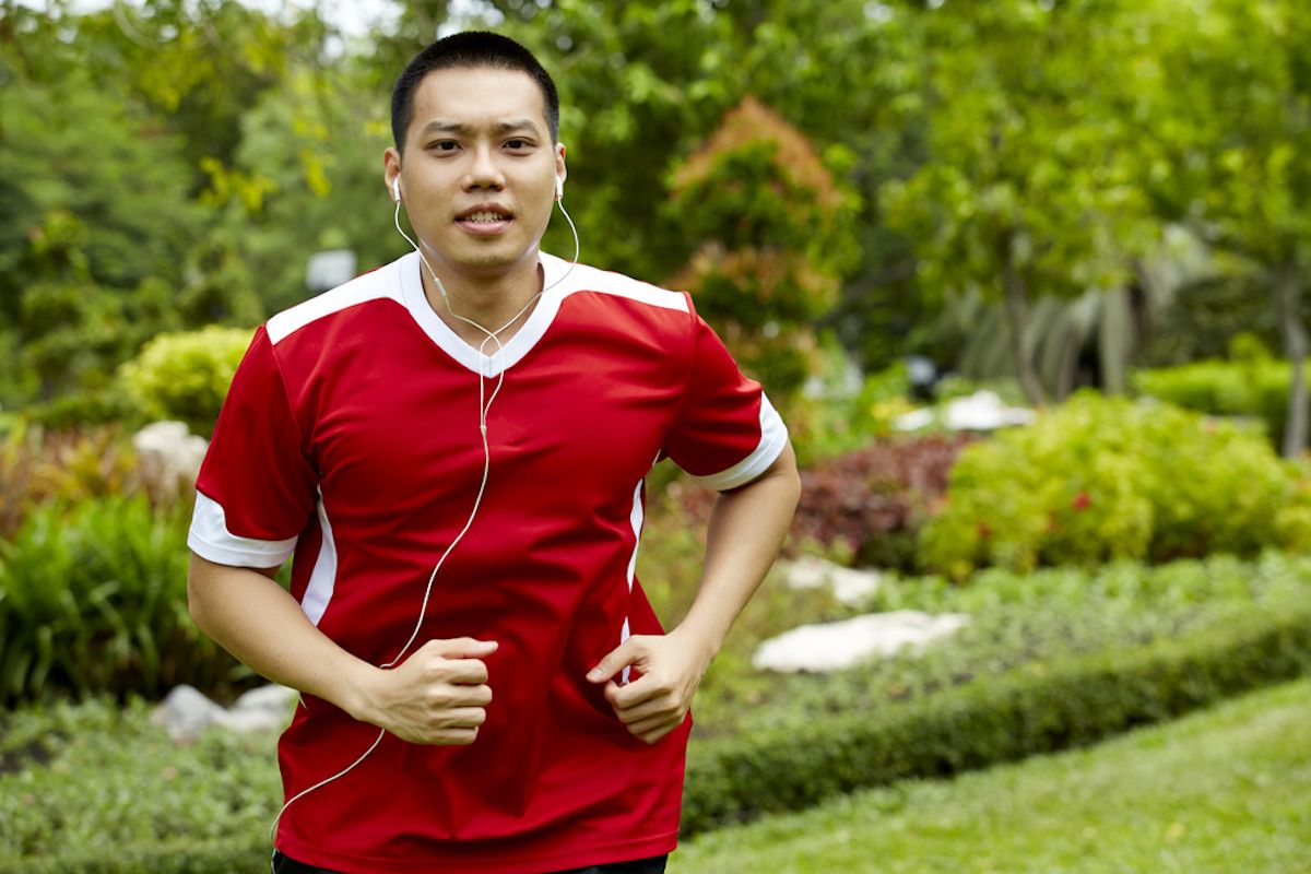 Người đàn ông châu Á đang chạy với tai nghe trong tai, mặc áo sơ mi thể thao màu đỏ