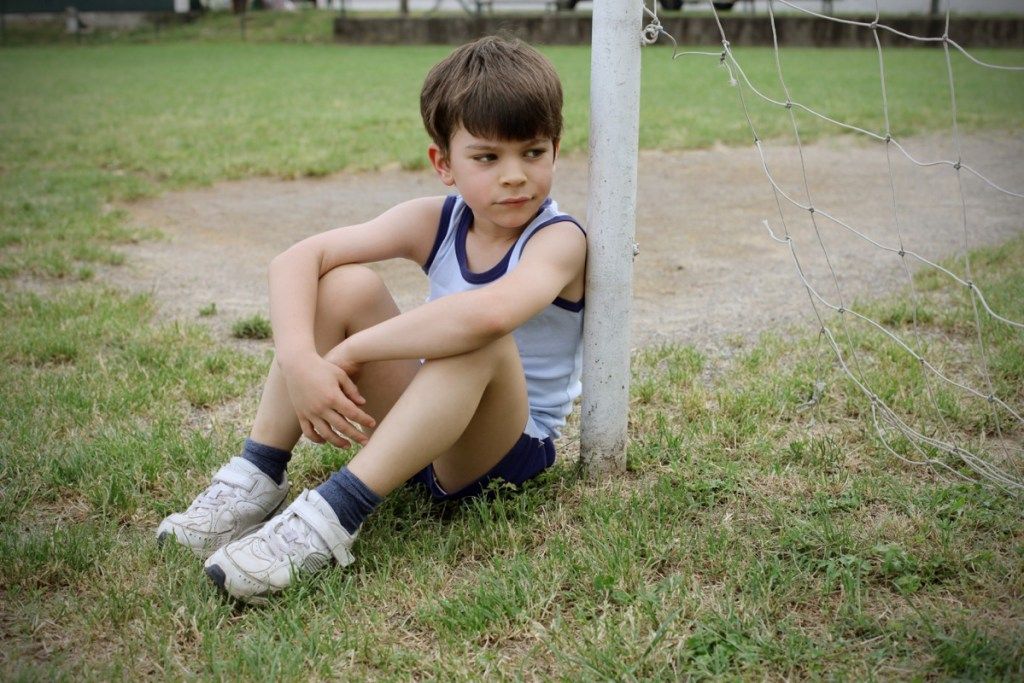 Surullinen lapsi pelaa jalkapalloa, huono vanhemmuus