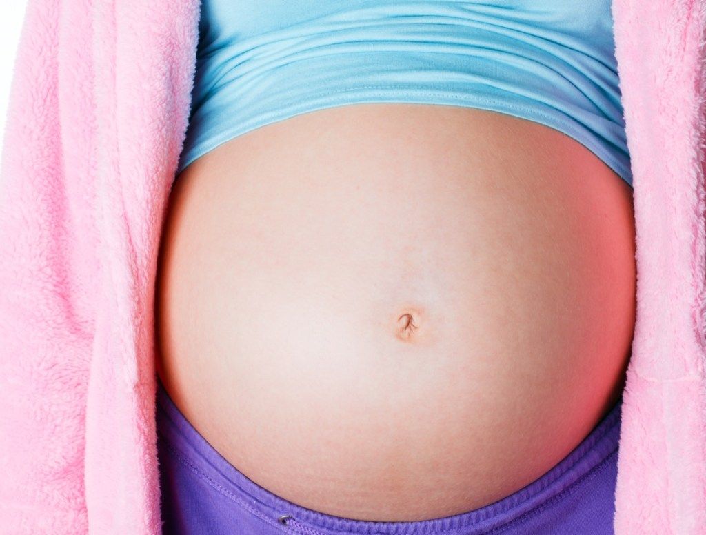 Detailní záběr na těhotné dospívající břicho s oříznutou košili a růžovým svetrem, co to je