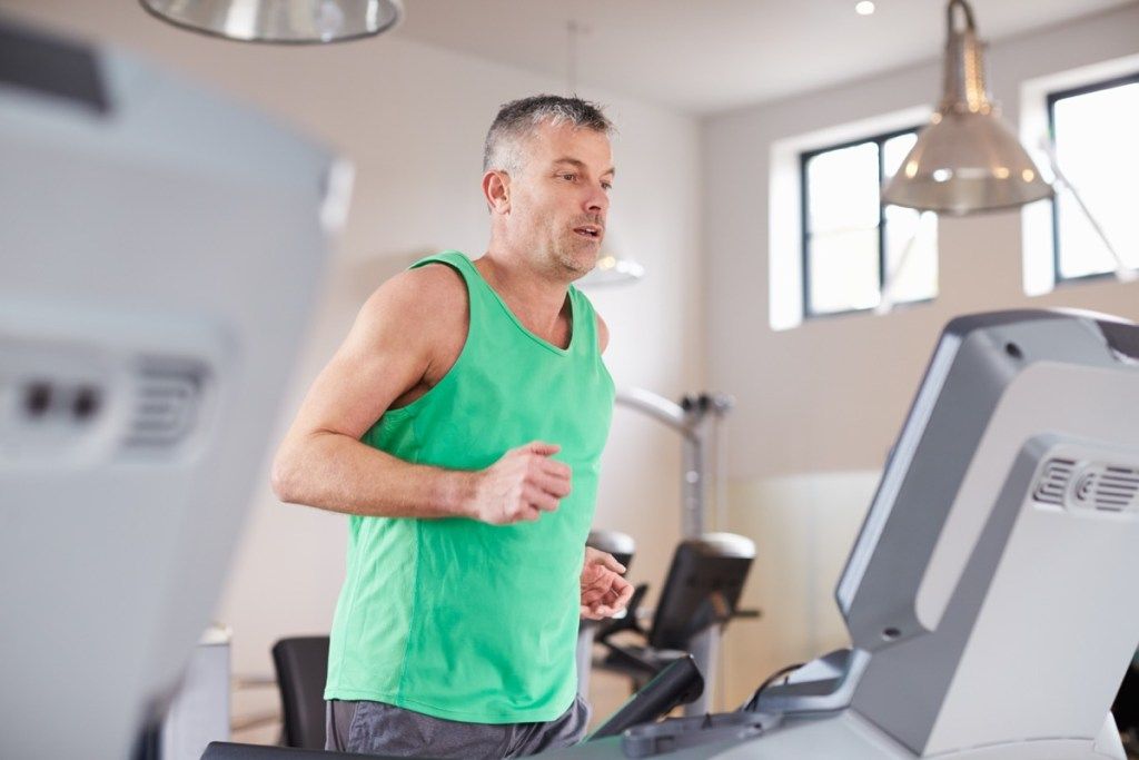 Pria kulit putih dewasa berlari dan melakukan kardio di treadmill
