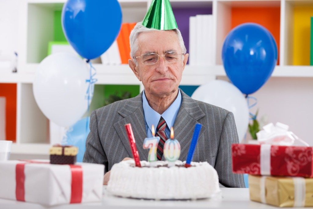 Anciano celebrando su 70 cumpleaños con aspecto confundido o triste