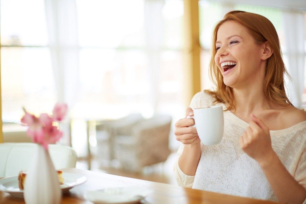 Femeie cu părul roșu care zâmbește și bea cafea
