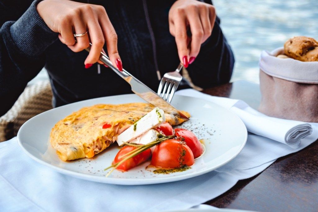 Žena jesť miešané vajcia, syr, paradajky a chlieb v reštaurácii pri vode