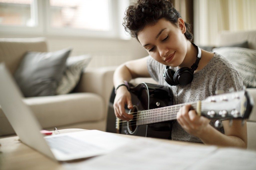 mladá dívka hraje na kytaru při pohledu na svůj počítač
