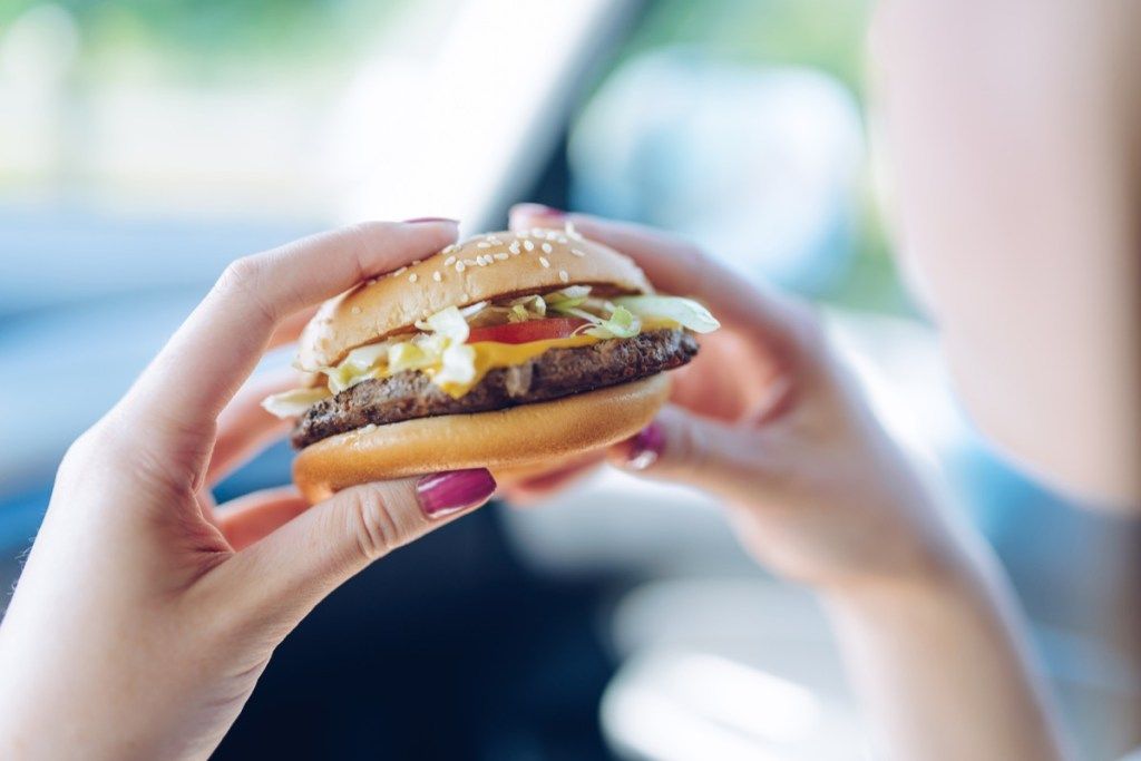 Meitene automašīnā tur ātrās ēdināšanas burgeru