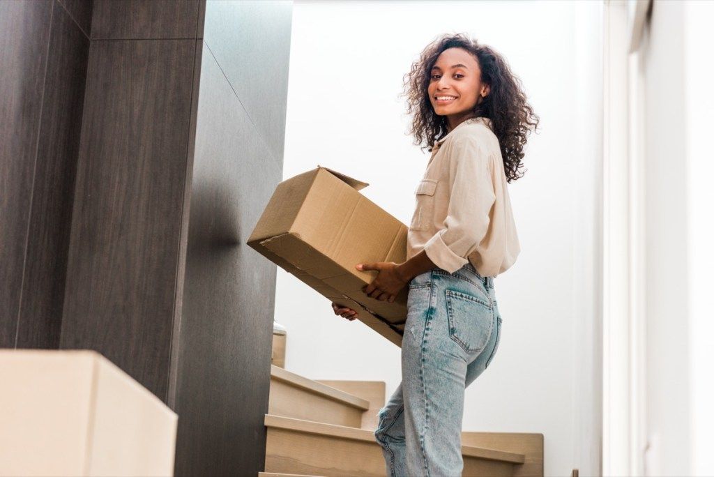 ung svart kvinna flyttar kartong på övervåningen