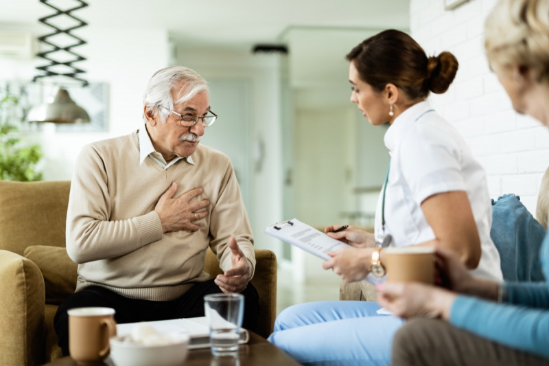   Възрастен мъж общува с лекар и се оплаква от болка в гърдите по време на домашно посещение.
