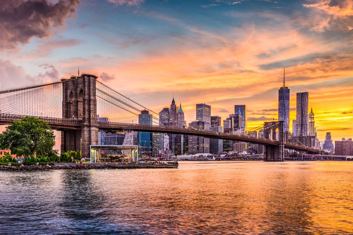 New York City Skyline op de East River met Brooklyn Bridge bij zonsondergang.